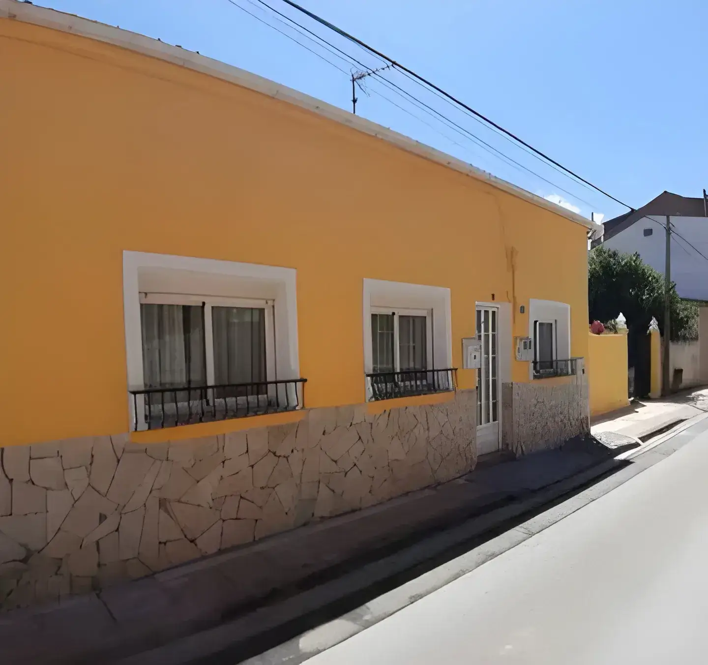 Los Pintores Leganés Fachada de casa tradicional pintada en color amarillo con zócalo de piedra